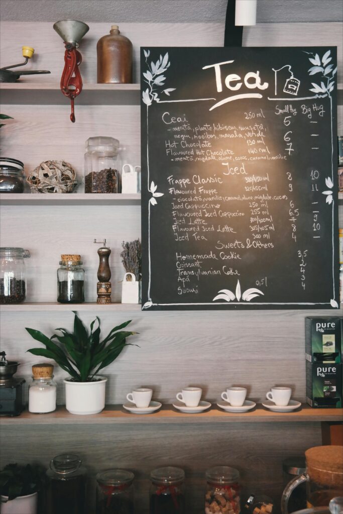 Cozy café interior with tea menu on chalkboard, cups and plants on wooden shelves.